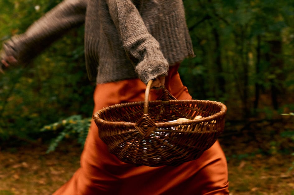 A woman carrying a woven basket through a forest